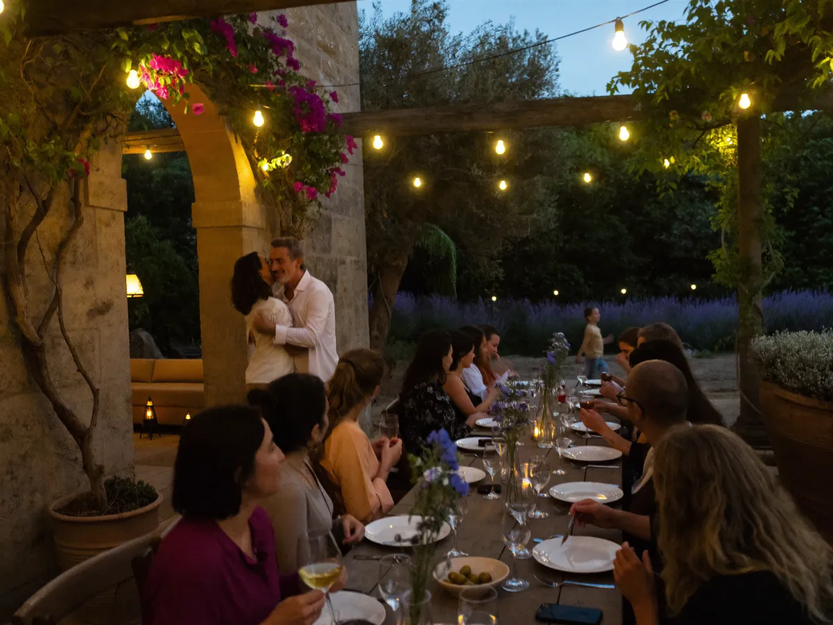 Invitados cenando bajo una pérgola con guirnaldas de luces; una pareja abrazada bajo un arco de piedra con buganvillas